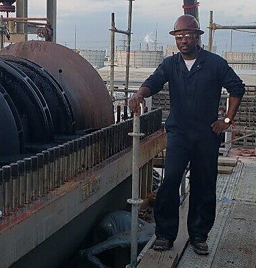 A man stands in protective gear next to a refining unit